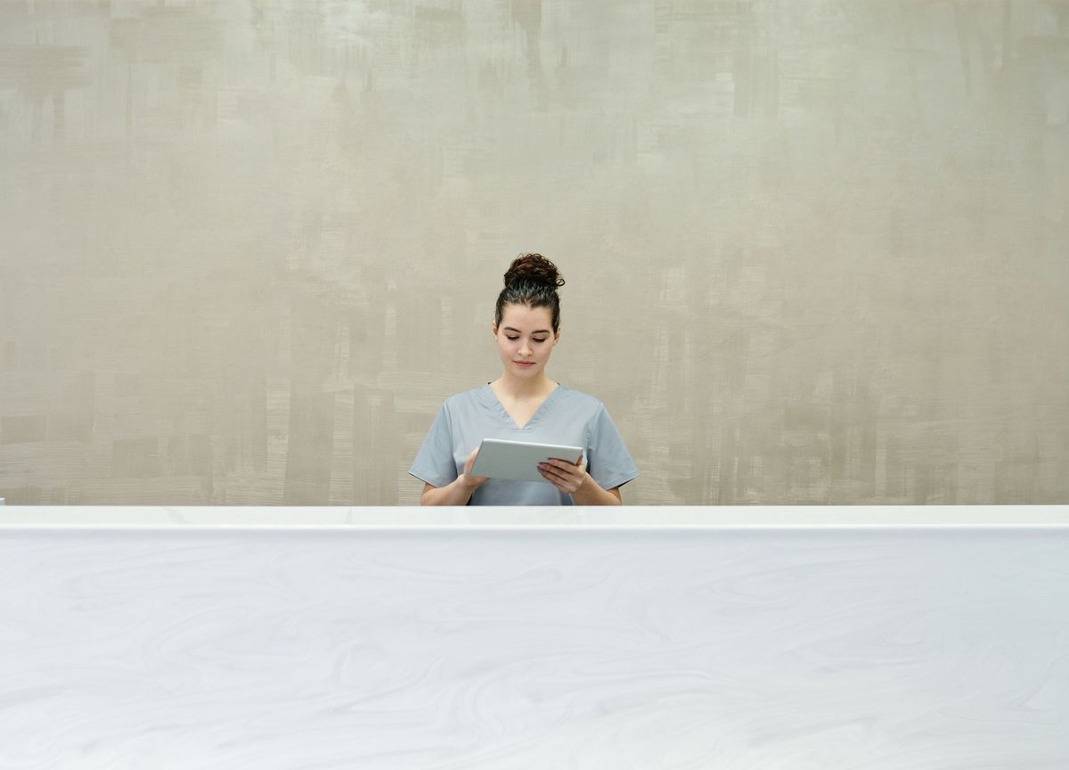 A member of practice staff at a reception desk, reading a tablet